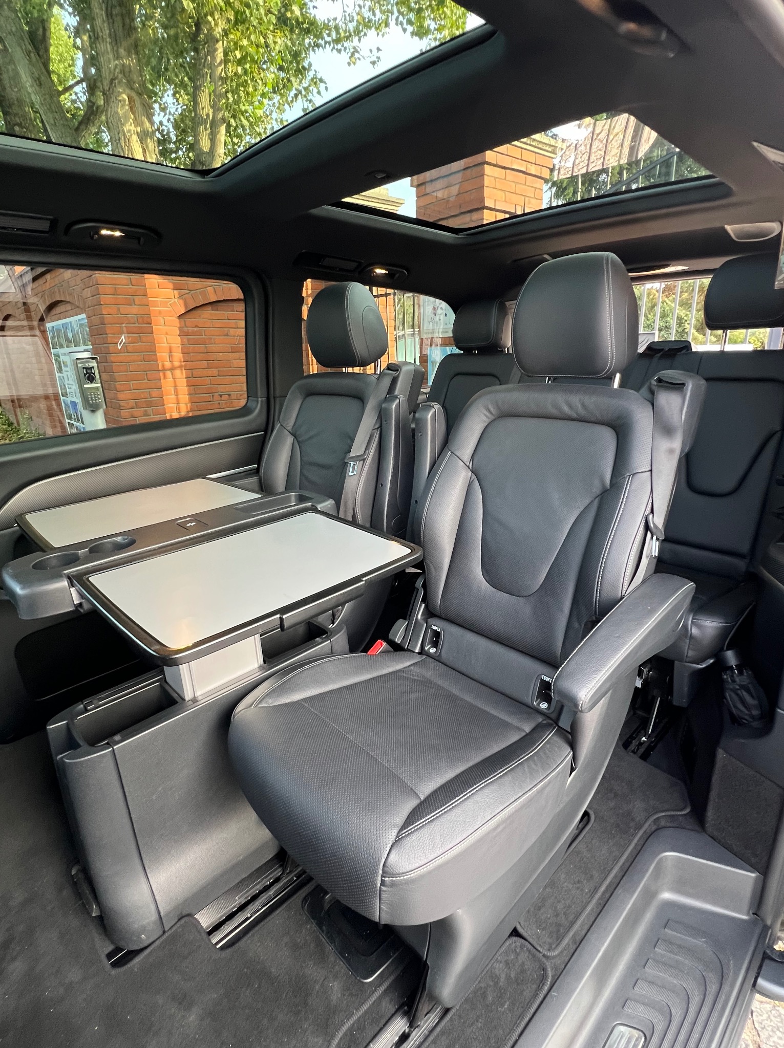 Wnętrze luksusowego busa z czarnymi skórzanymi fotelami, rozkładanymi stolikami i panoramicznym oknem dachowym, widok z perspektywy pasażera.