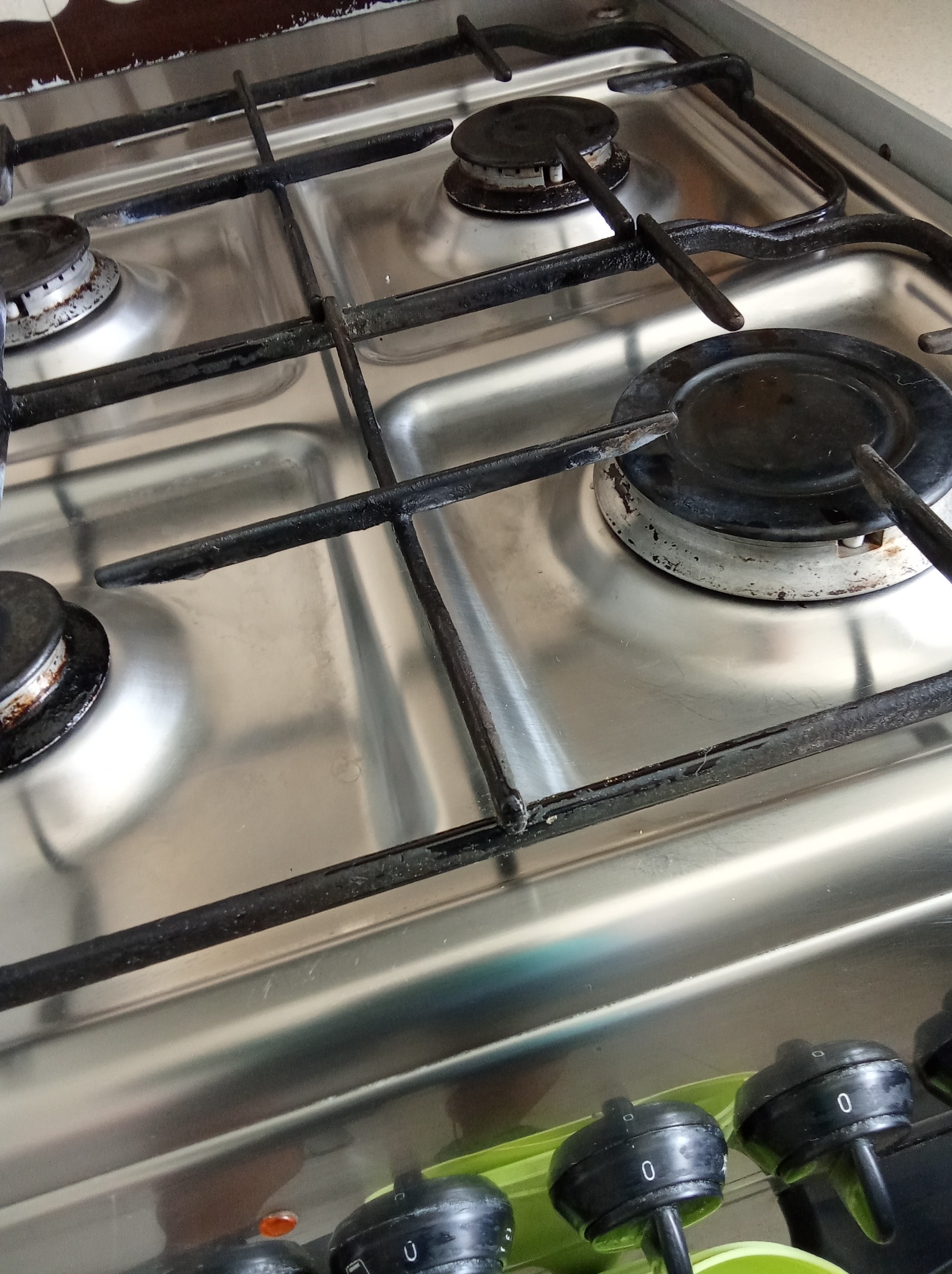 Metalowa kuchenka gazowa z czterema palnikami, widoczne czarne ruszty i pokrętła. Powierzchnia płyty jest czysta i błyszcząca, co sugeruje niedawne sprzątanie.