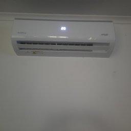 Klimatyzacja-Klima-Cool Jarek Pałka - Biała klimatyzacja Aura Line Inverter zamontowana na ścianie. Widoczny wyświetlacz z temperaturą 20 stopni Celsjusza. Ujęcie z dołu.