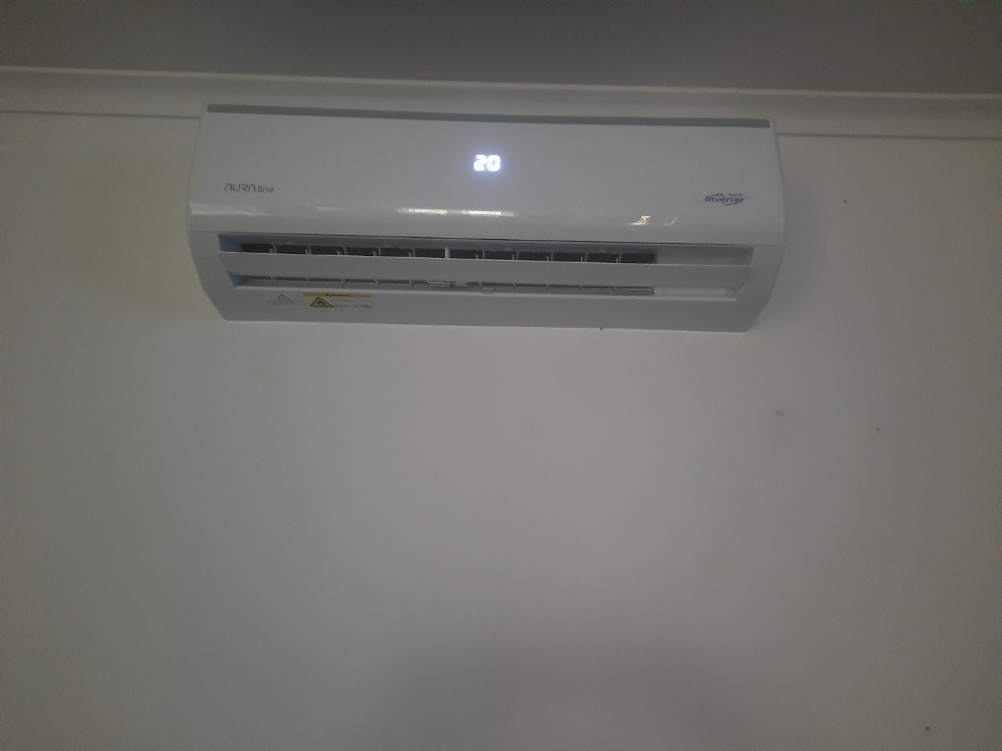 Biała klimatyzacja Aura Line Inverter zamontowana na ścianie. Widoczny wyświetlacz z temperaturą 20 stopni Celsjusza. Ujęcie z dołu.