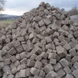 Kupa szarych, kubicznych kamieni na tle wiejskiego krajobrazu z drzewami i pagórkami w pochmurny dzień.