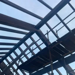 Konstrukcja drewniana dachu w trakcie budowy, widziana z dołu na tle jasnego nieba. Widoczne rusztowanie.