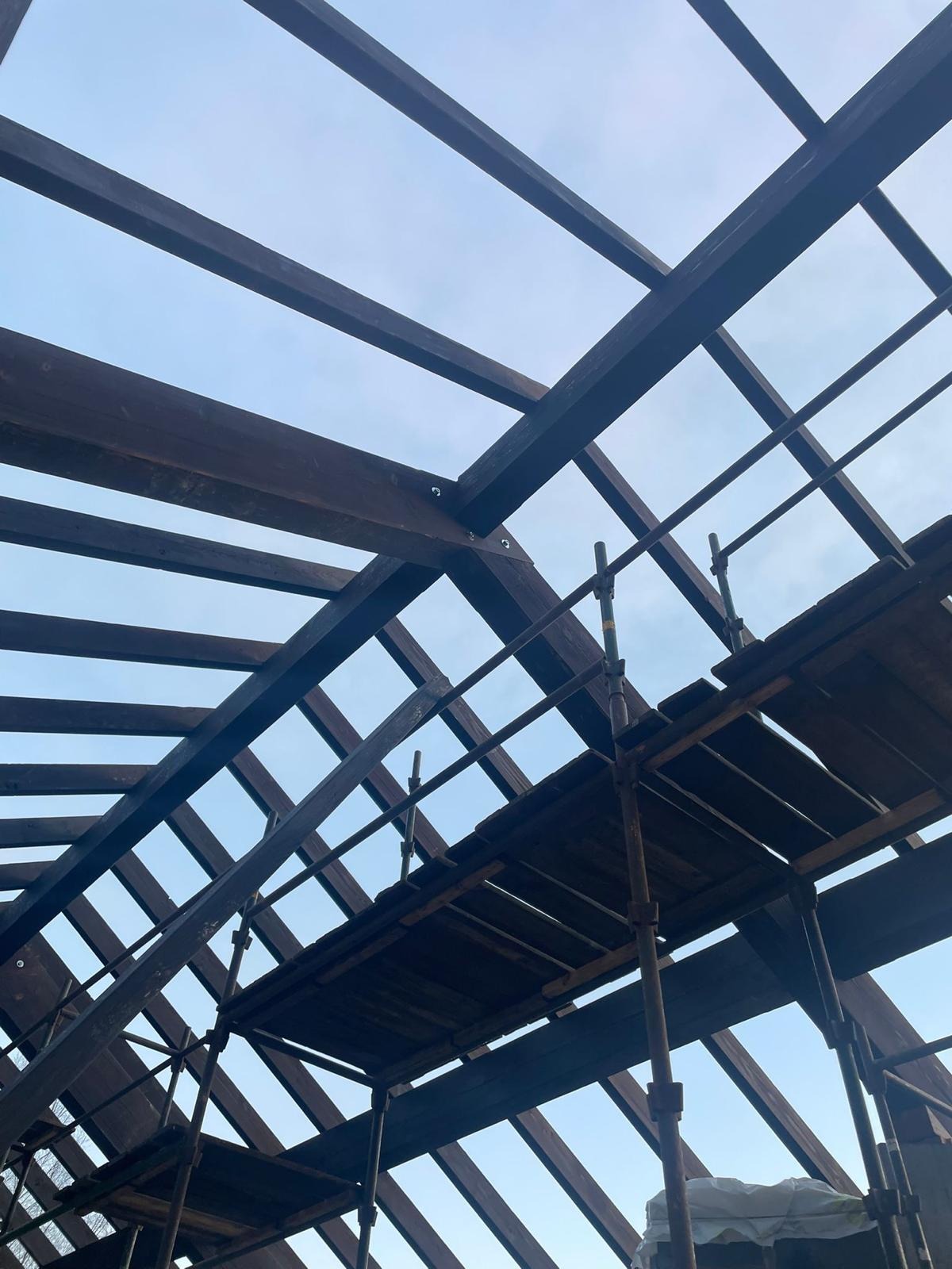 Konstrukcja drewniana dachu w trakcie budowy, widziana z dołu na tle jasnego nieba. Widoczne rusztowanie.