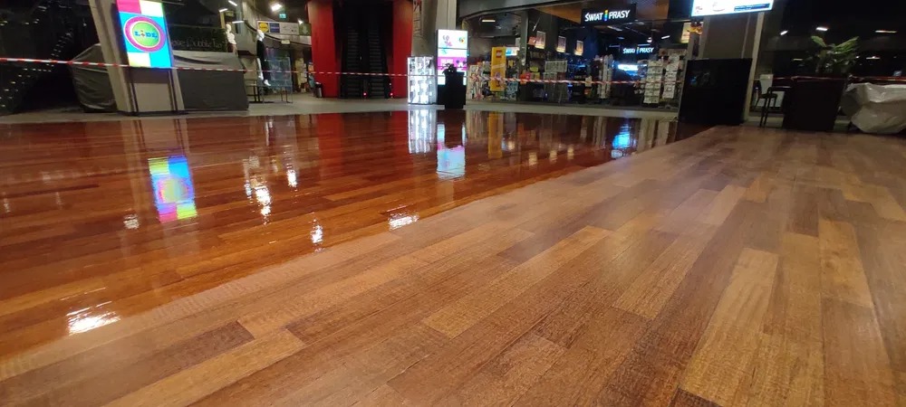 Podłoga drewniana w centrum handlowym, połowa powierzchni po renowacji z wyraźnym połyskiem, druga połowa matowa, przed renowacją.