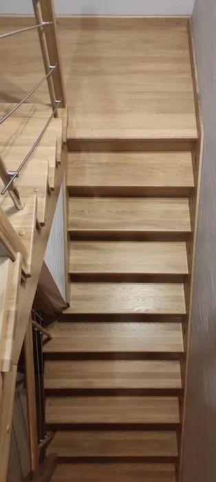 Widok z góry na drewniane schody po renowacji, z widoczną metalową balustradą i jasnym odcieniem drewna.