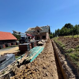 SIMPLE FLAT SPÓŁKA Z OGRANICZONĄ ODPOWIEDZIALNOŚCIĄ - Budowa domu jednorodzinnego w trakcie realizacji: widoczny stan surowy otwarty, dach w budowie, wykop pod fundamenty, materiały budowlane składowane na placu budowy.