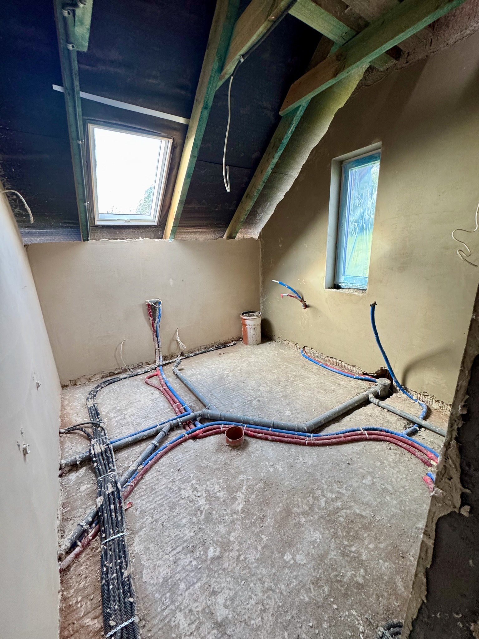 Poddasze w trakcie prac instalacyjnych: widoczne rury CO i instalacja elektryczna na surowym podłożu, okno dachowe i okno w ścianie szczytowej. Ściany w stanie surowym.