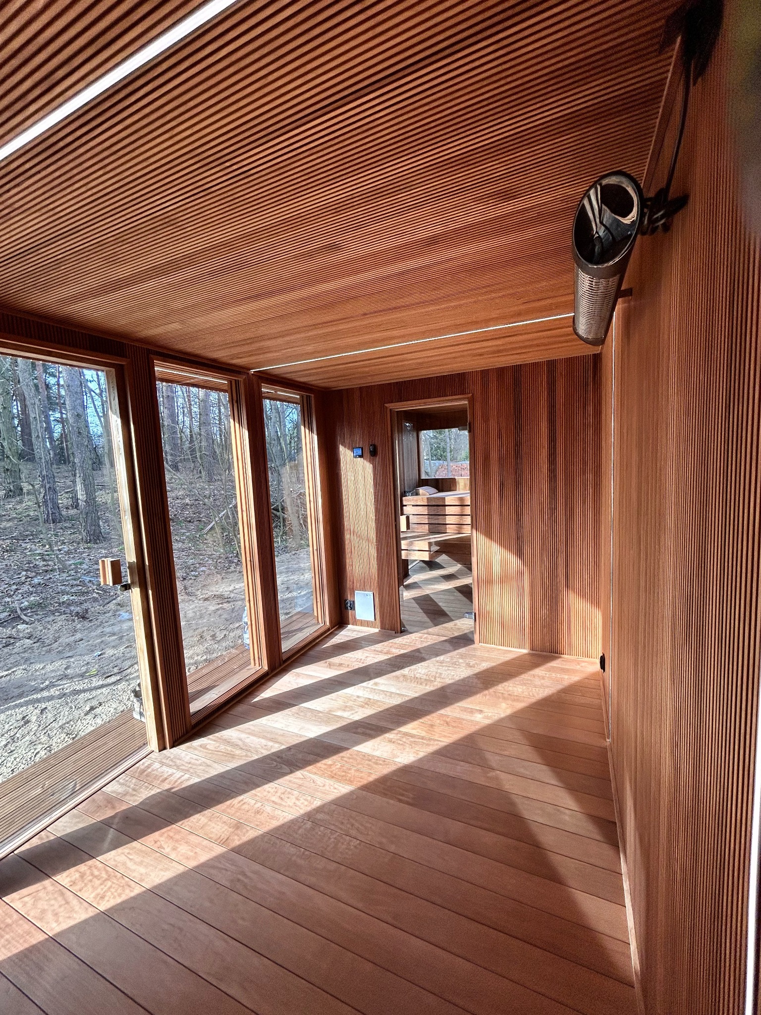 Wnętrze drewnianej kabiny z przeszkloną ścianą i widokiem na las, z charakterystycznym oświetleniem i drewnianymi panelami ściennymi.