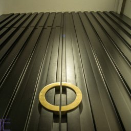 Kuchnie na wymiar Warszawa DMKUCHNIE - Ciemna, pionowo żłobkowana szafa z okrągłym, złotym uchwytem, widziana z dołu, z logo firmy w lewym dolnym rogu.