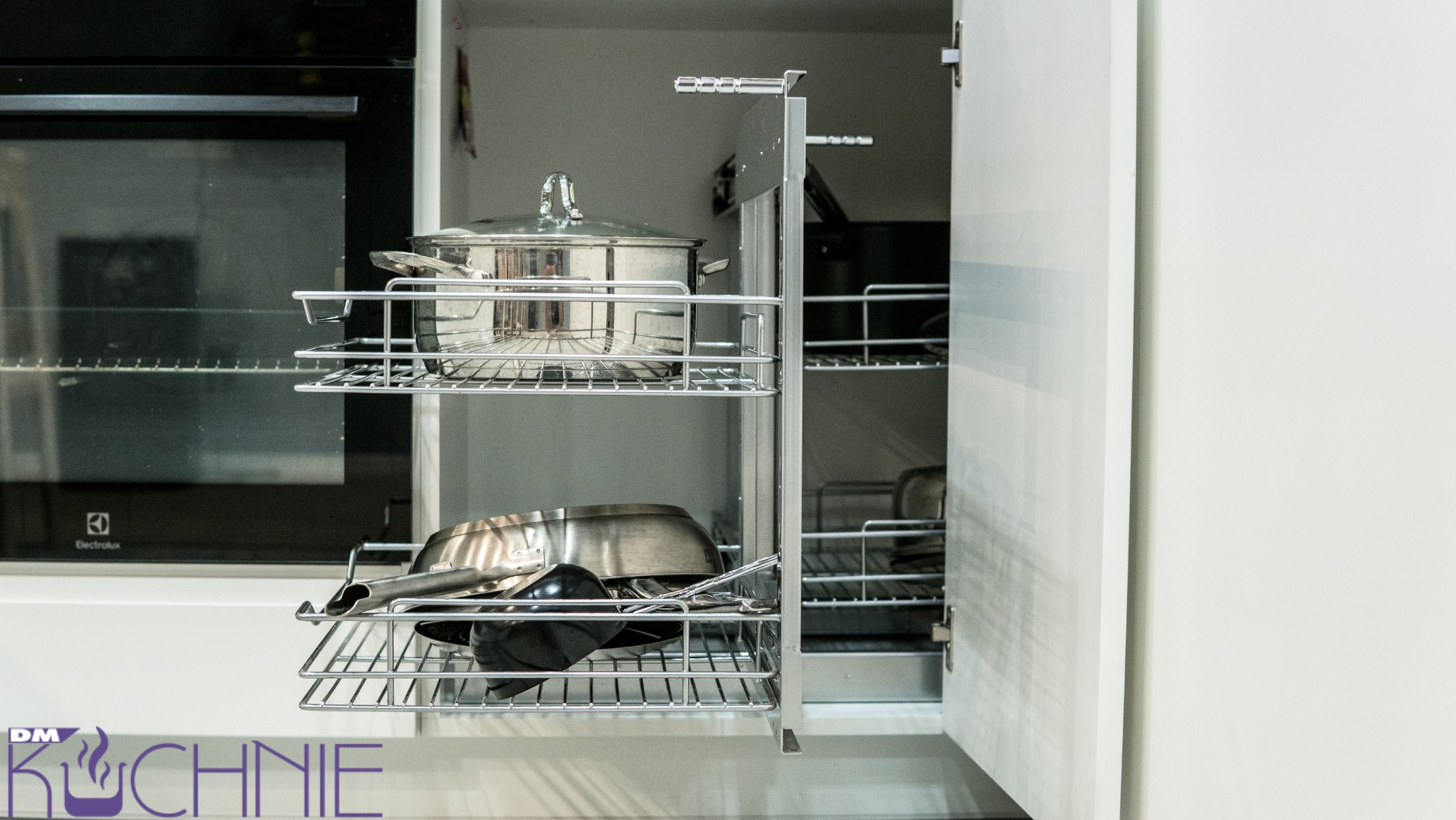 Wysuwana szafka cargo w białej kuchni z garnkami i patelniami, widoczny piekarnik Electrolux w tle.