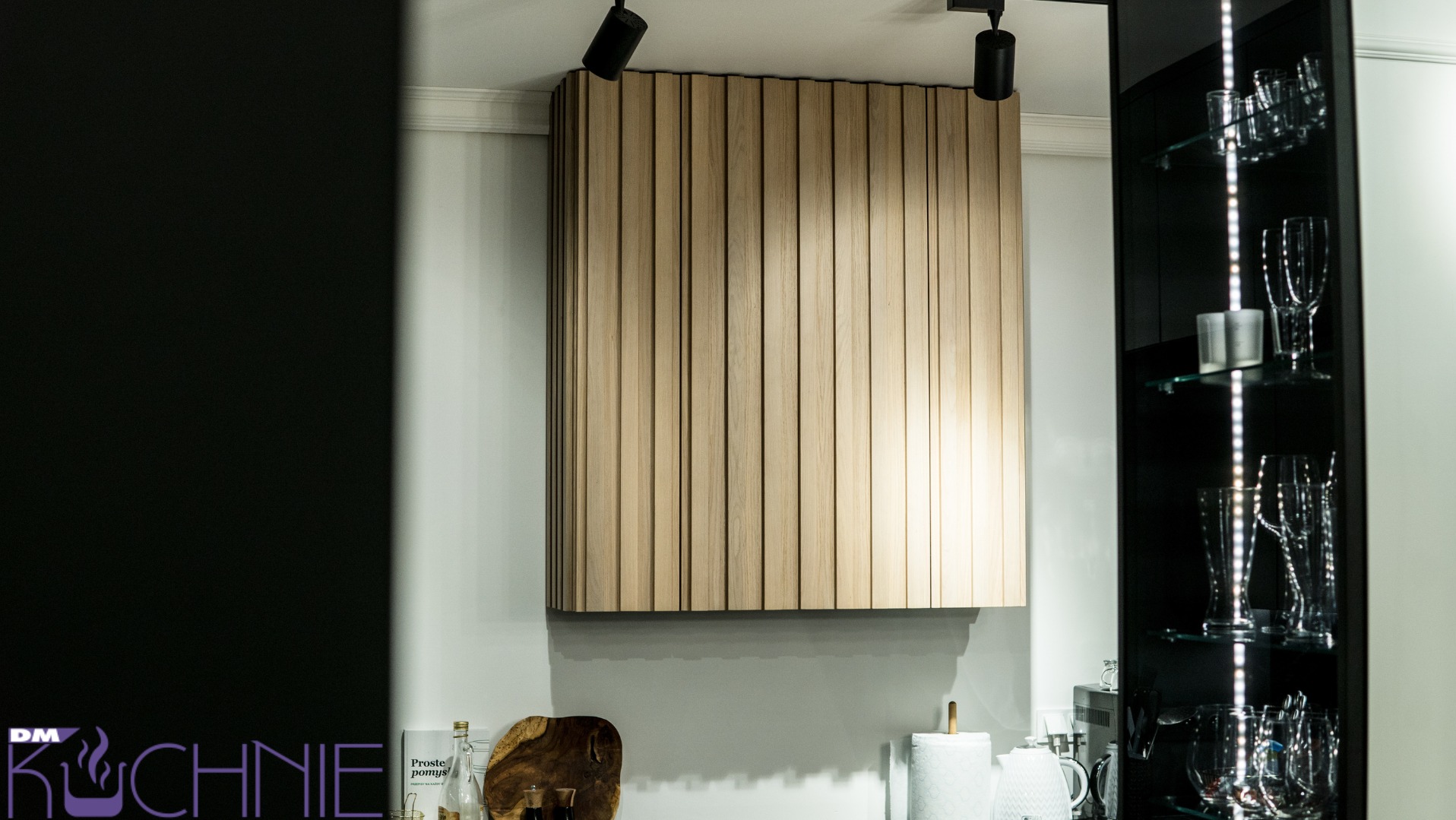 Nowoczesna kuchnia z drewnianą okładziną ścienną z pionowych listew i przeszkloną szafką z podświetleniem LED oraz szkłem dekoracyjnym.