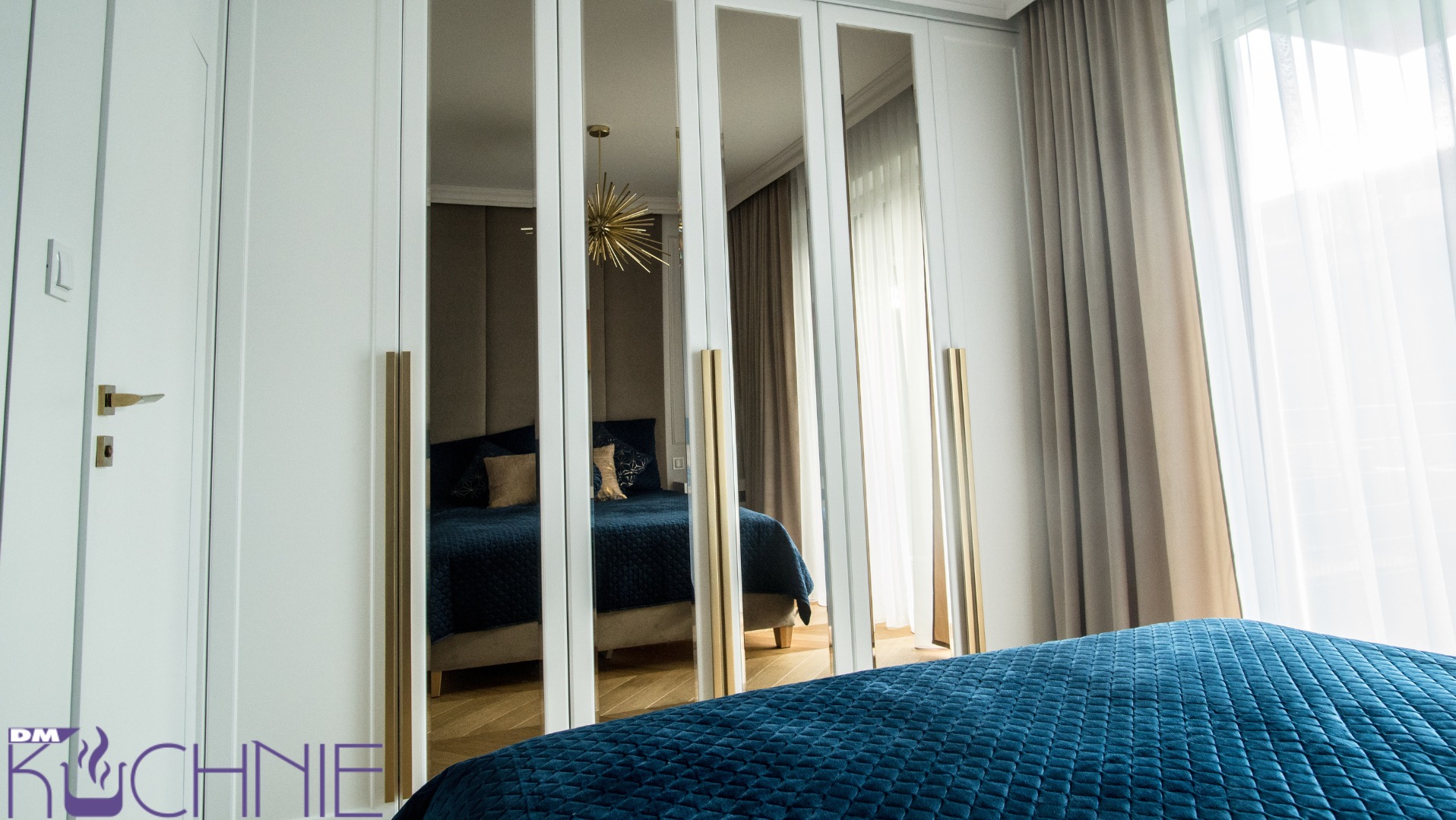 Biała szafa wnękowa z lustrzanymi drzwiami, odbijająca wnętrze sypialni z niebieskim łóżkiem i złotym żyrandolem.