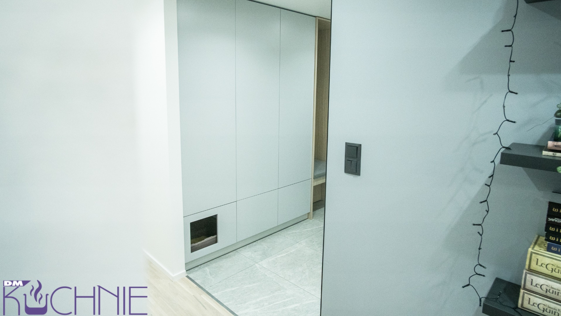 Nowoczesna szafa wnękowa z szarymi frontami i małą wnęką dla zwierząt, widoczna z perspektywy wnętrza w mieszkaniu w Warszawie.