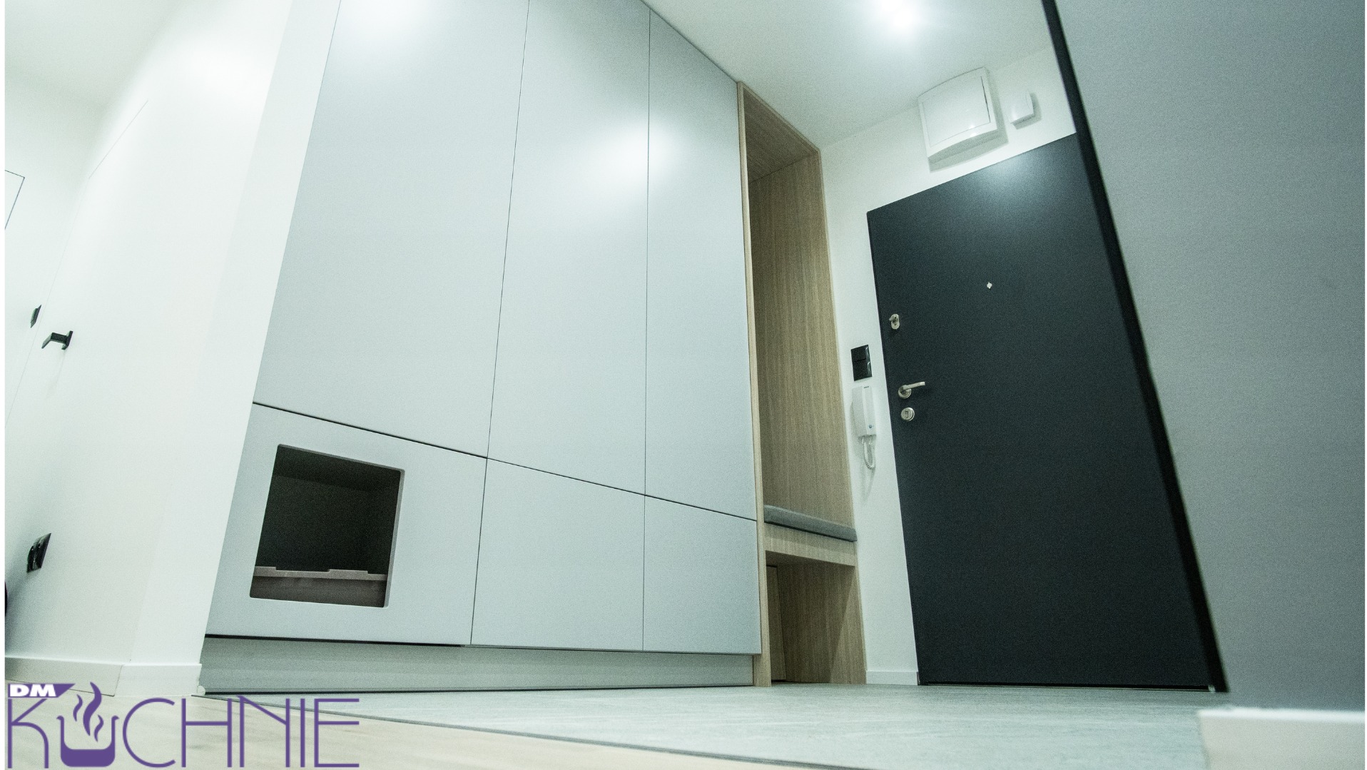 Nowoczesna zabudowa przedpokoju z szafami w kolorze jasnej szarości, wnęką z siedziskiem z drewnianym wykończeniem i czarnymi drzwiami wejściowymi.