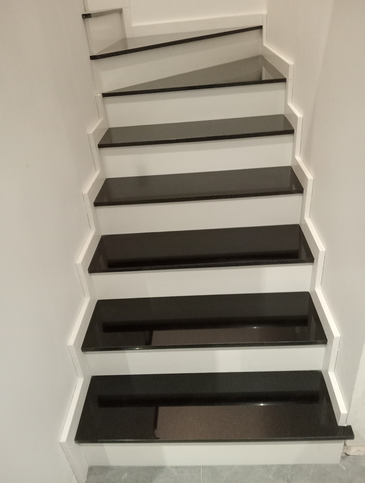 Białe schody z czarnymi, błyszczącymi stopniami kamiennymi. Minimalistyczny design, widok z dołu, jasne oświetlenie, gładka powierzchnia stopni.