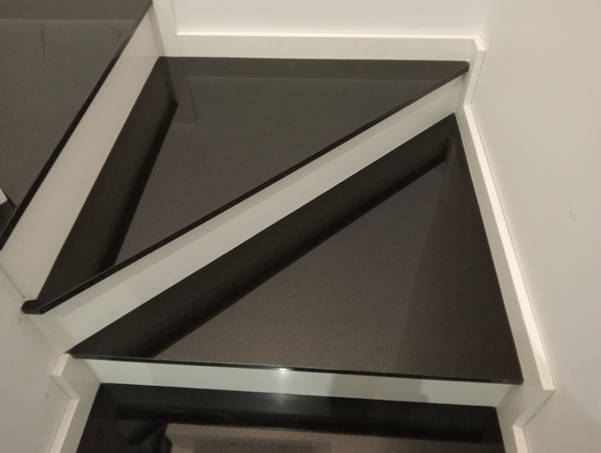 Nowoczesne schody kamienne z czarnymi stopniami i białymi elementami wykończeniowymi, widok z góry, minimalistyczny design.