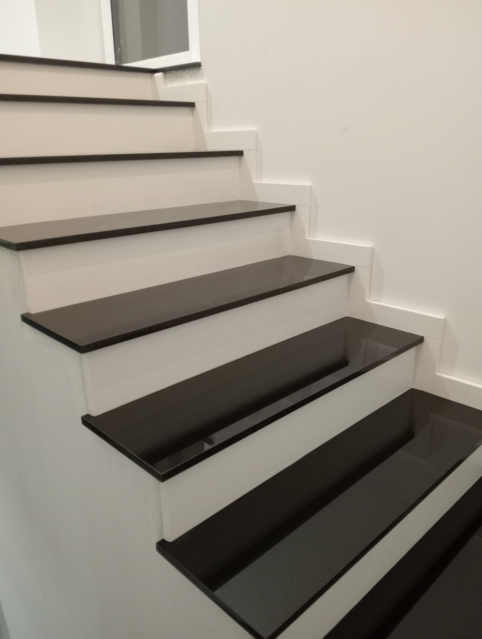 Nowoczesne schody z czarnymi stopniami i białymi podstopnicami, widok z dołu, gładkie powierzchnie, minimalizm.