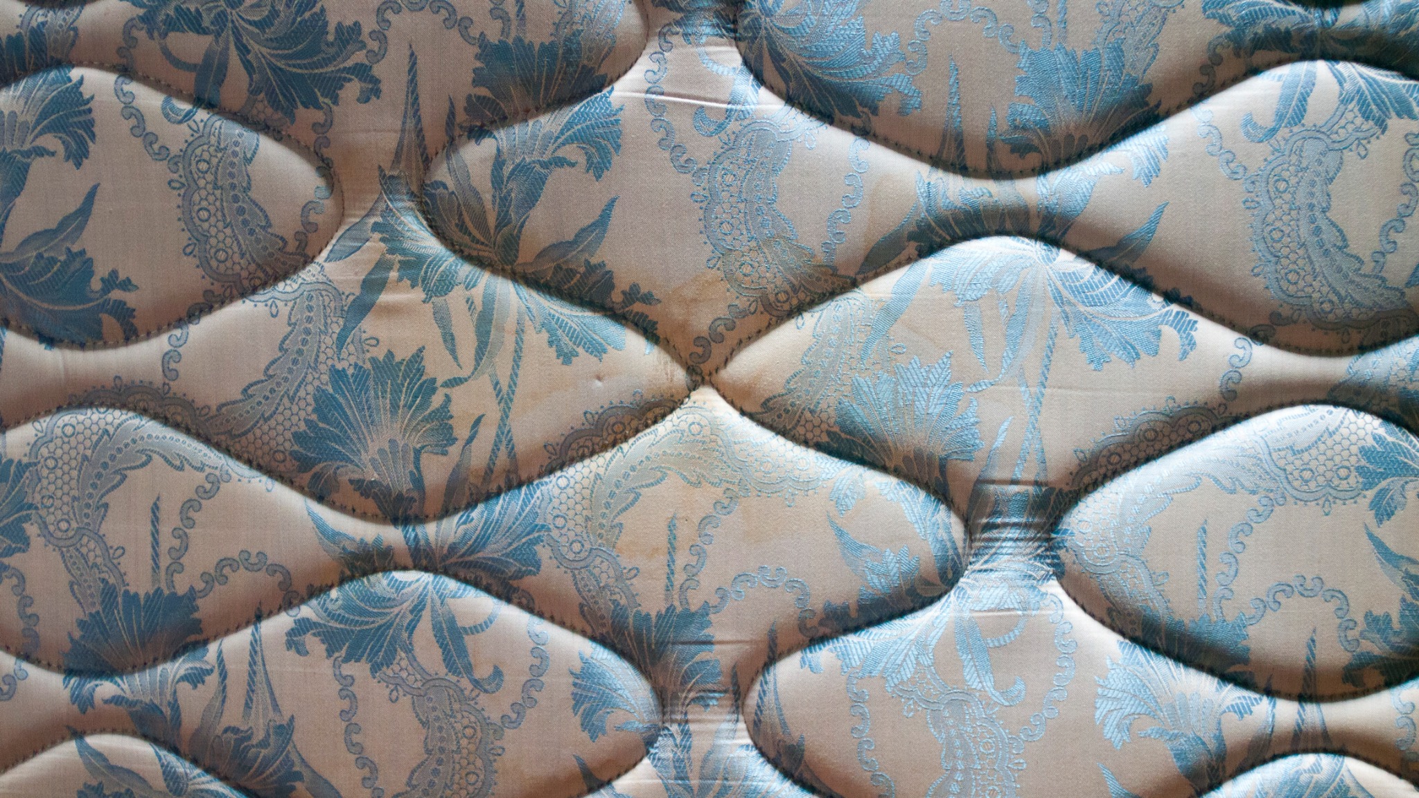 Materac z kremowo-błękitnym wzorem kwiatowym i pikowaniem tworzącym wypukłości.