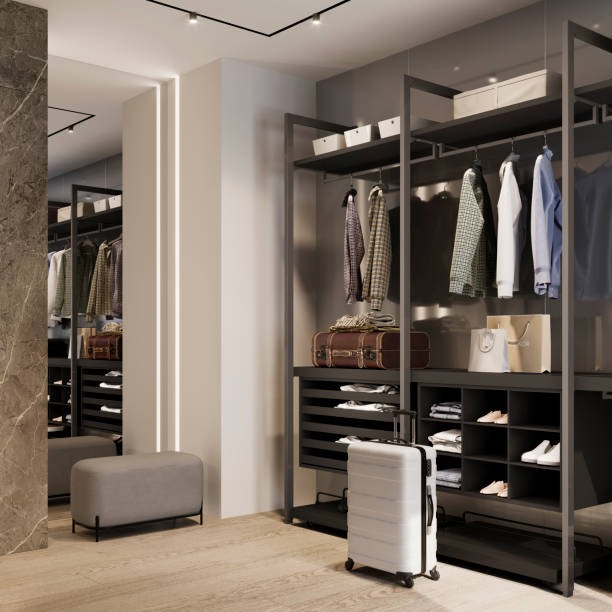 Nowoczesna garderoba z szarą zabudową, oświetleniem punktowym i lustrem, z widoczną walizką, pufą i uporządkowanymi ubraniami.