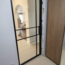 Stalove Tarnobrzeg Łukasz Załucki - Szklane drzwi w czarnej metalowej ramie z widocznym wnętrzem mieszkania i częściowo wykończonym ościeżem.