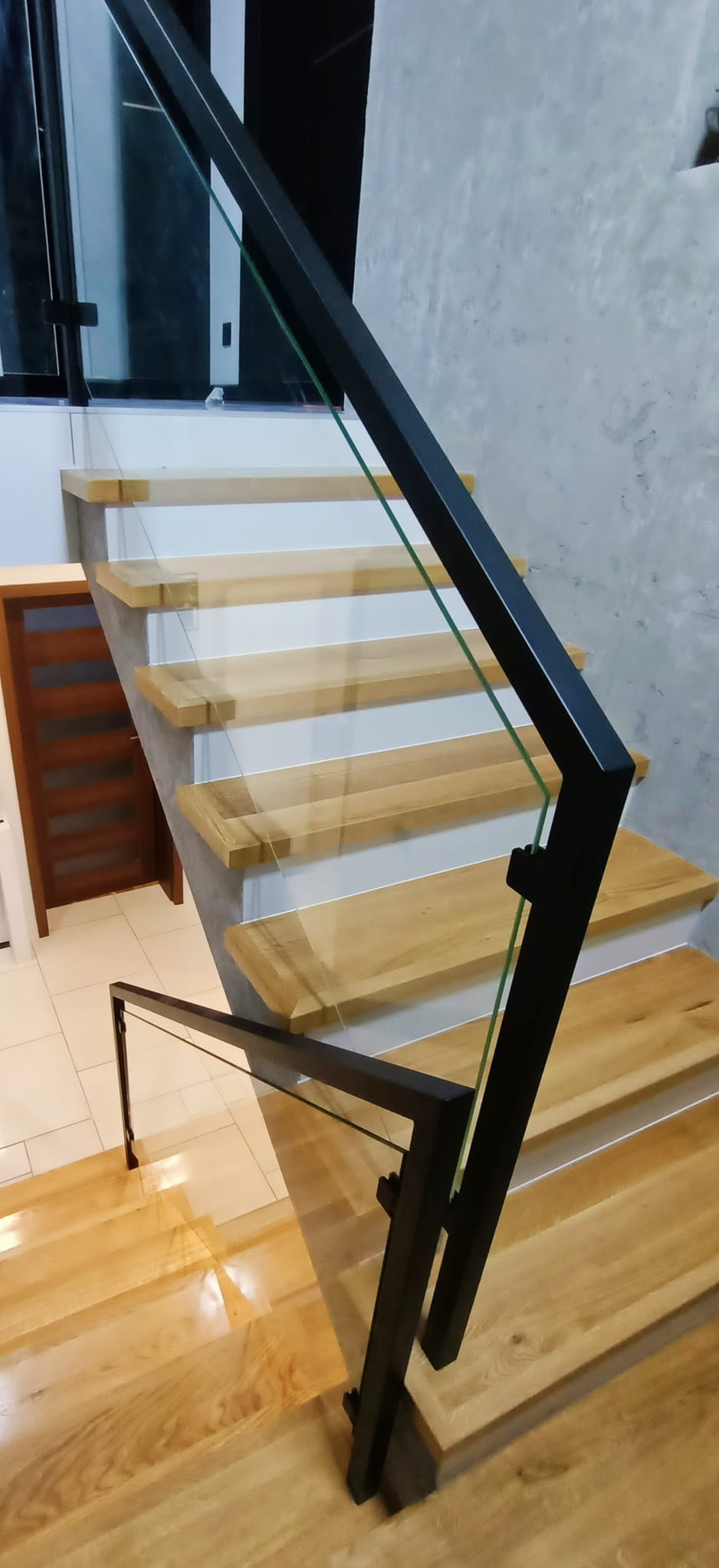 Schody drewniane z czarną, metalową poręczą i szklanymi panelami, widok z góry, minimalistyczny design.