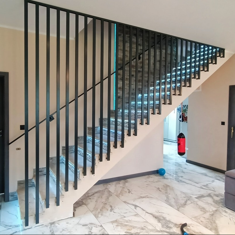 Schody wewnętrzne z czarną, pionową balustradą z metalowych prętów, podświetleniem LED na ścianie i marmurową posadzką.