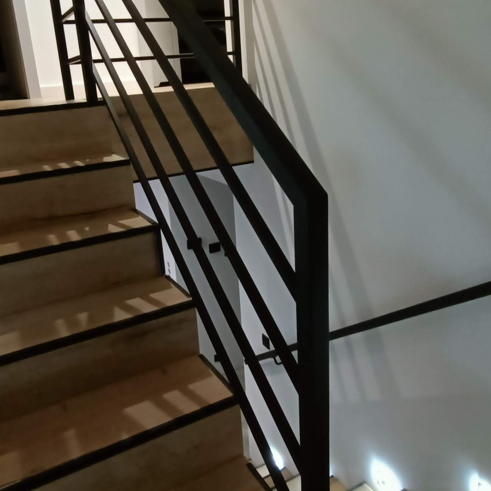 Schody z drewnianymi stopniami i czarną, minimalistyczną poręczą z prostych, pionowych prętów, widok z góry.