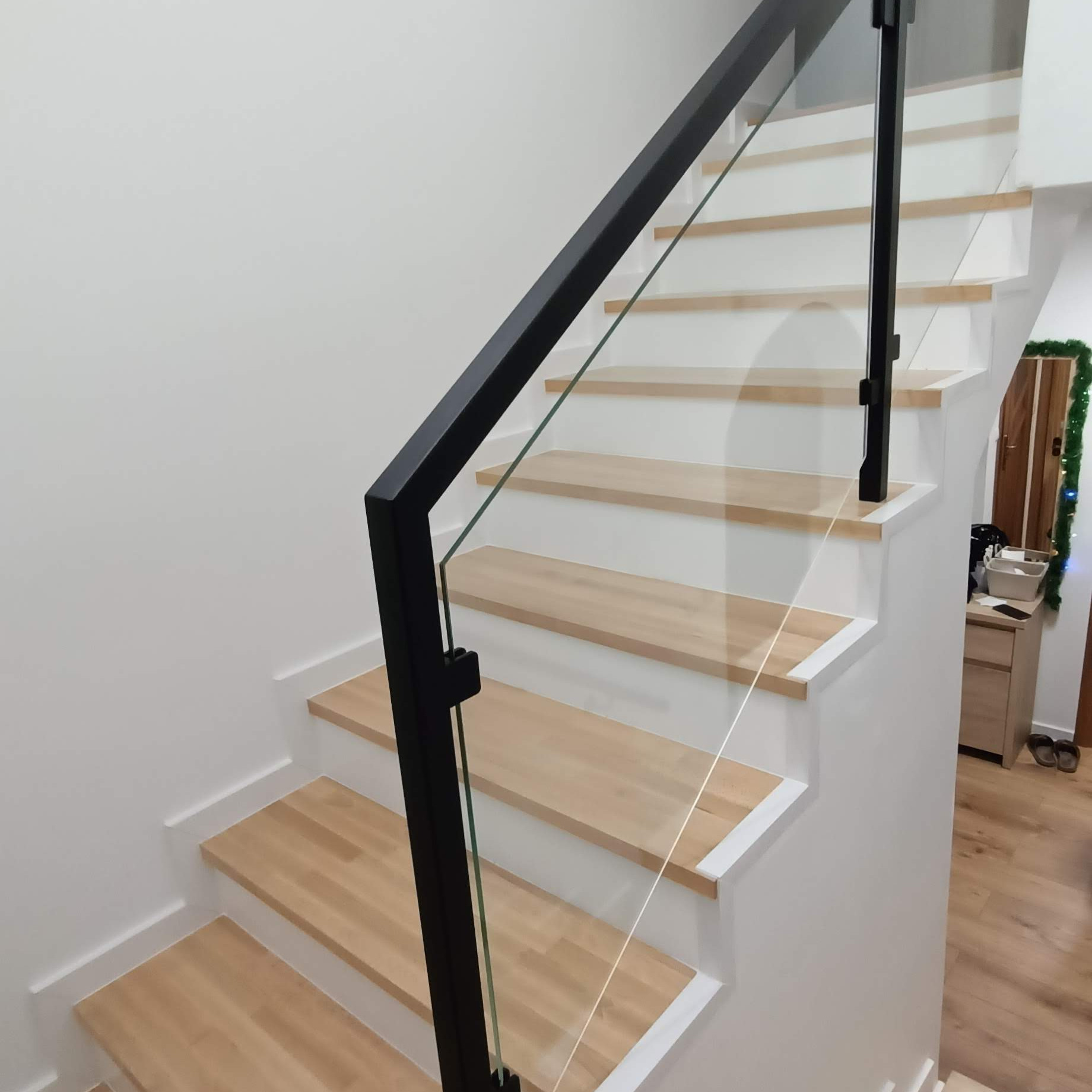 Schody drewniane z balustradą ze szkła i czarnych, metalowych słupków, widok z dołu, minimalistyczny design.