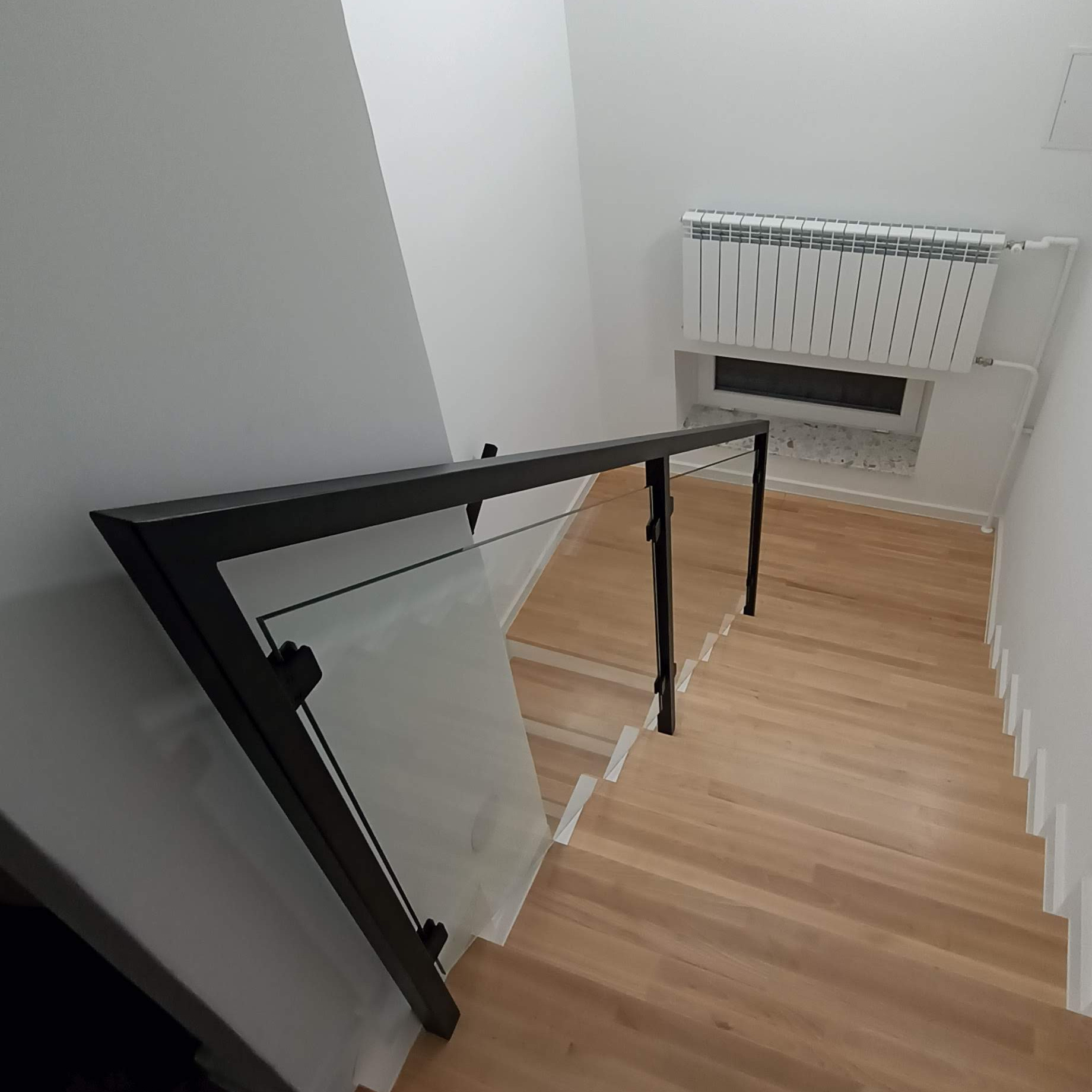 Wewnętrzne schody z drewnianymi stopniami i nowoczesną szklaną balustradą z czarnymi elementami mocującymi, widok z góry, Tarnobrzeg.