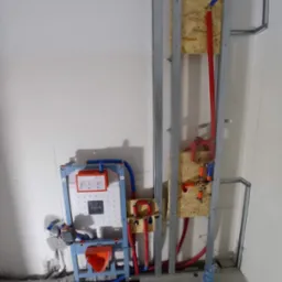 Stelaż podtynkowy WC marki Vitra zamontowany w konstrukcji z profili, widoczne podłączenia hydrauliczne z rur PEX w kolorach czerwonym i niebieskim, oraz butelka wody na podłodze.