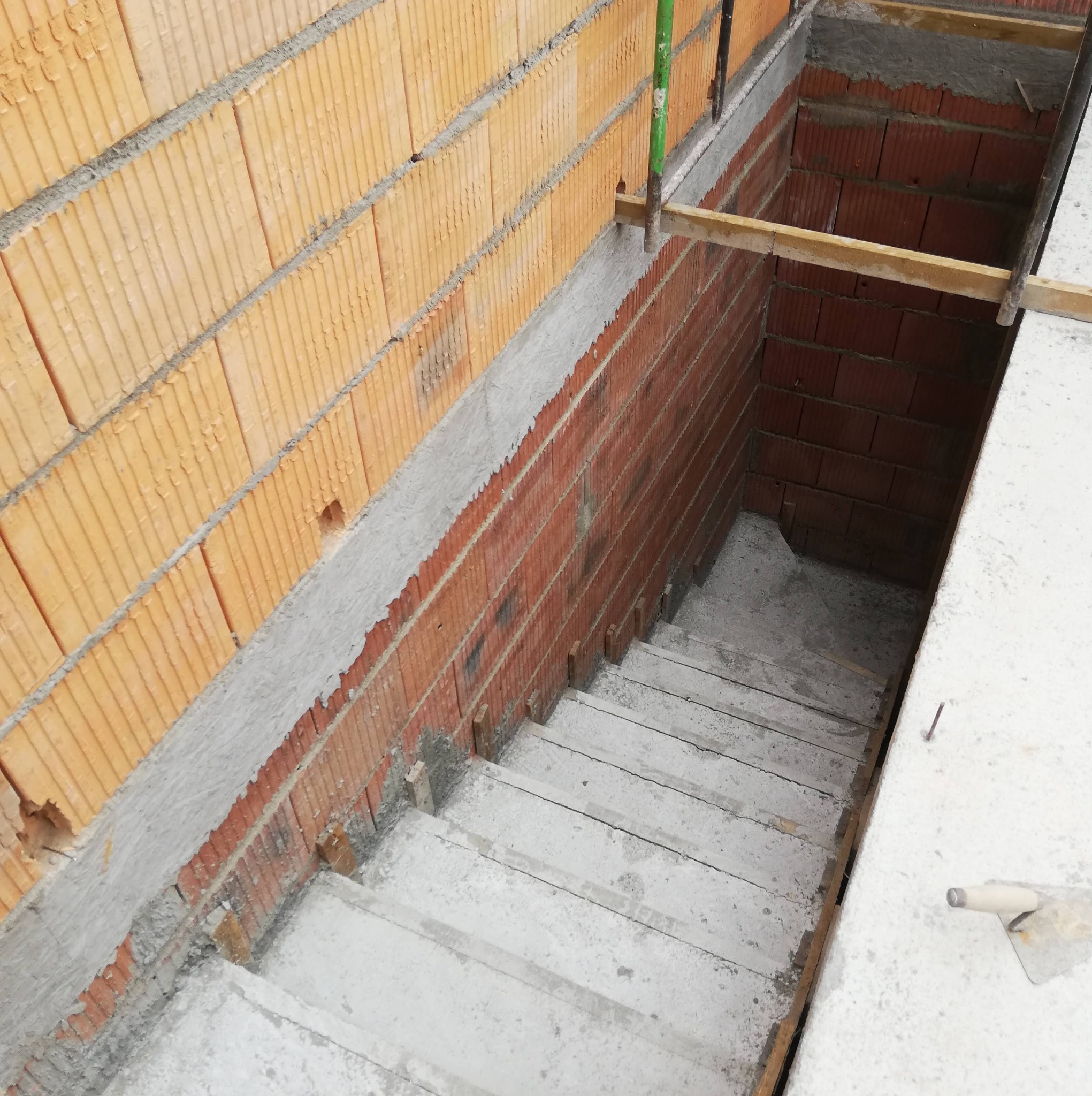 Wykop pod schody do piwnicy z wymurowanymi ścianami z bloczków ceramicznych, widoczne drewniane stemple podtrzymujące konstrukcję.