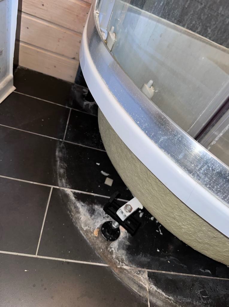 Niedokładnie posprzątana czarna podłoga po montażu kabiny prysznicowej z widocznymi pozostałościami po silikonie i drobnych elementach montażowych.