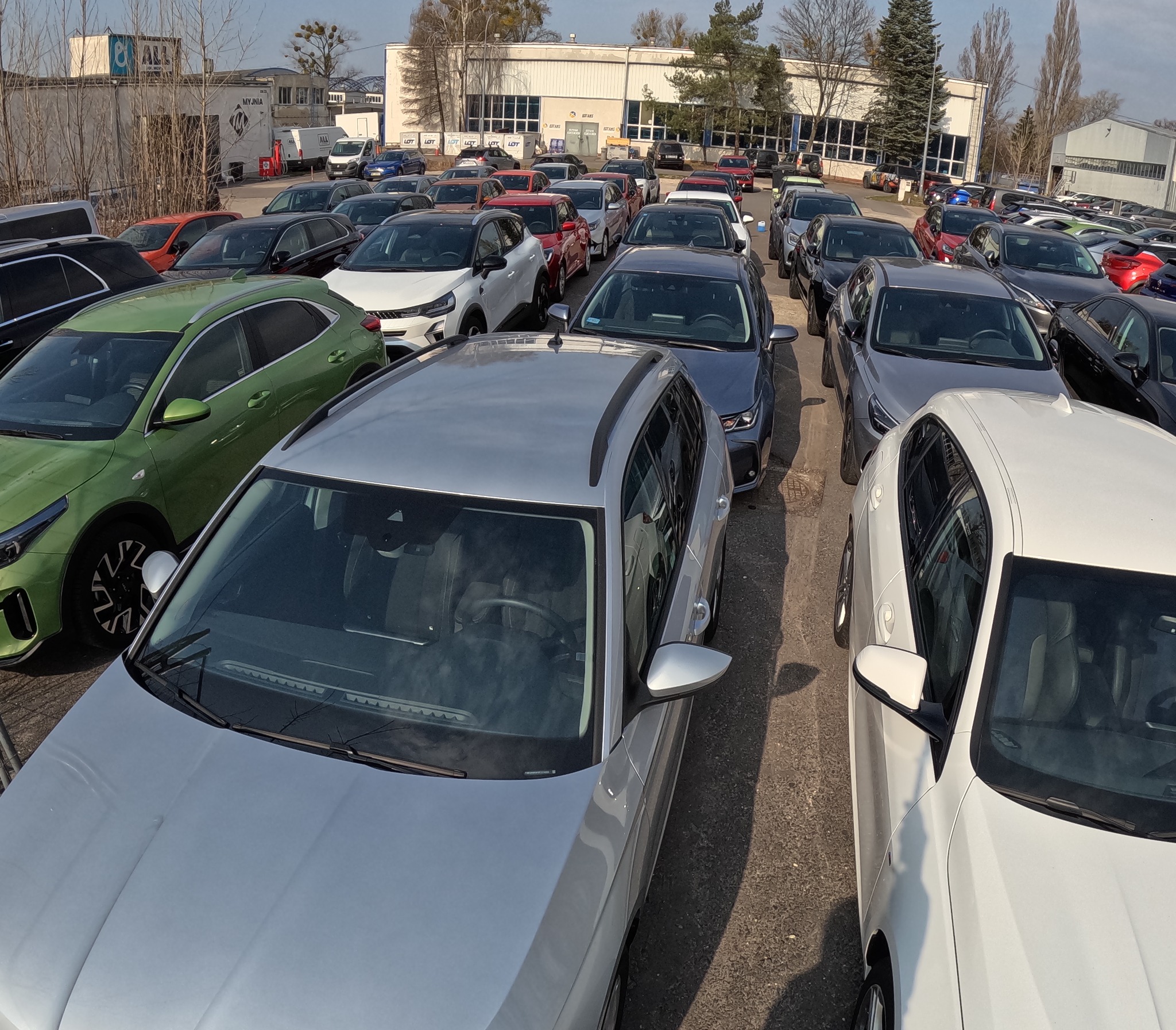 Duży parking samochodowy w Warszawie, wypełniony różnymi modelami i kolorami aut, widok z góry na srebrny samochód na pierwszym planie.