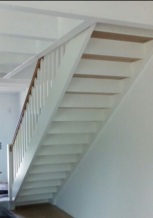 Białe schody drewniane z brązową poręczą, widok z dołu, minimalistyczny design. Schody bez wykończenia stopni, widoczne surowe drewno.