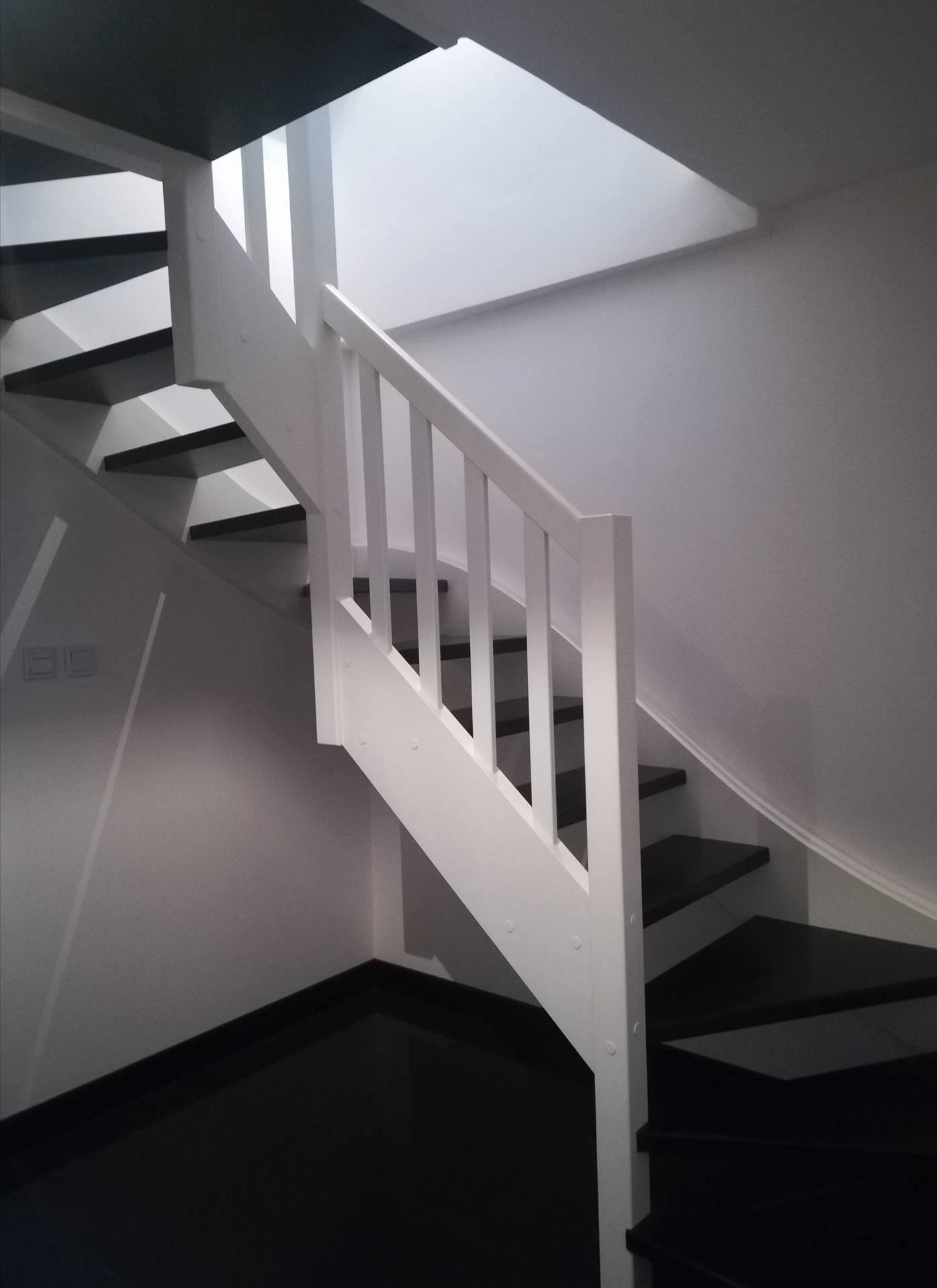 Nowoczesne schody z czarnymi stopniami i białą balustradą. Minimalistyczny design z subtelnym oświetleniem górnym, tworzący elegancką przestrzeń.