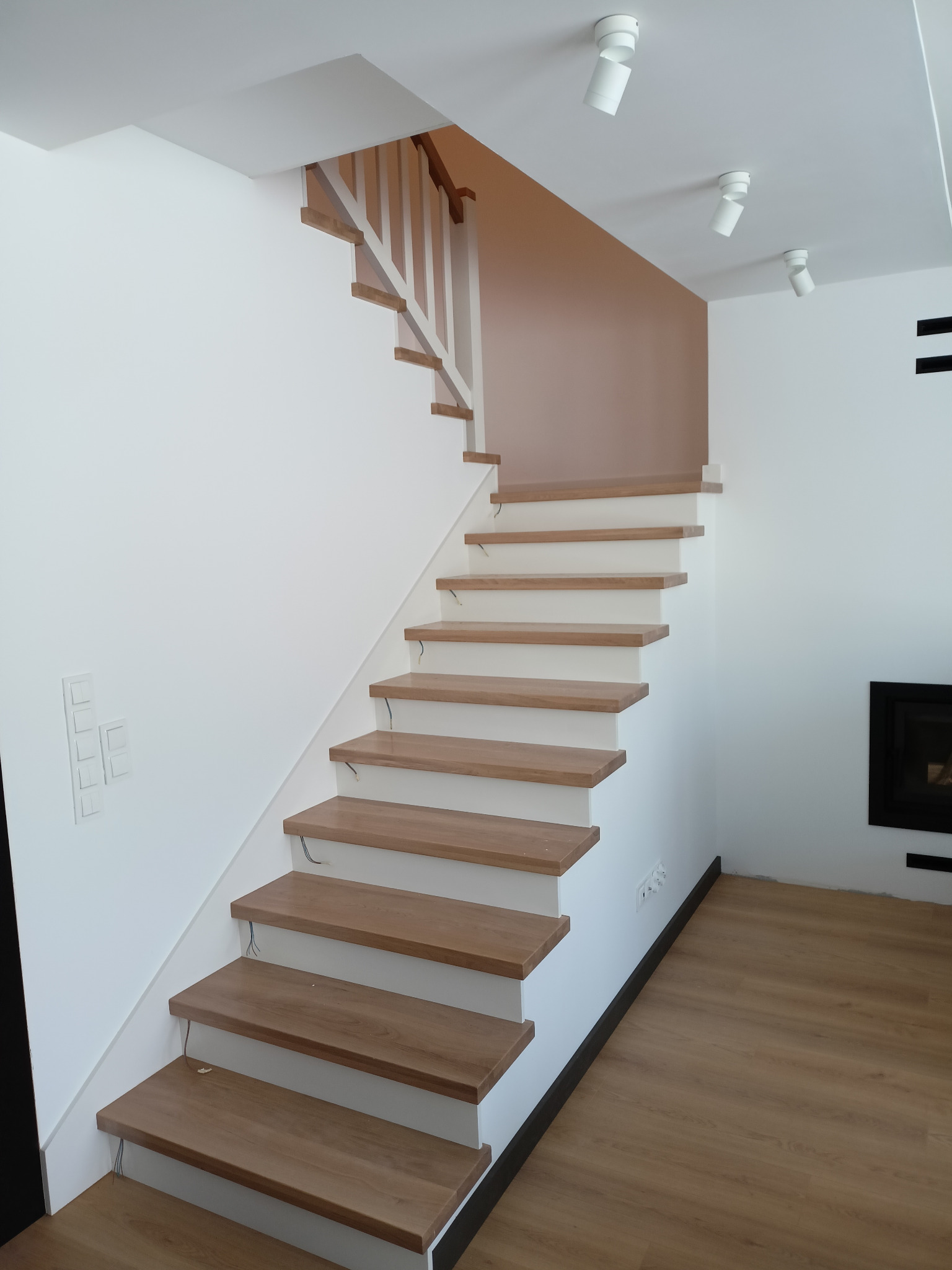 Nowoczesne schody z drewnianymi stopniami i białą balustradą w jasnym wnętrzu z oświetleniem punktowym, widok z dołu na bieg schodów.