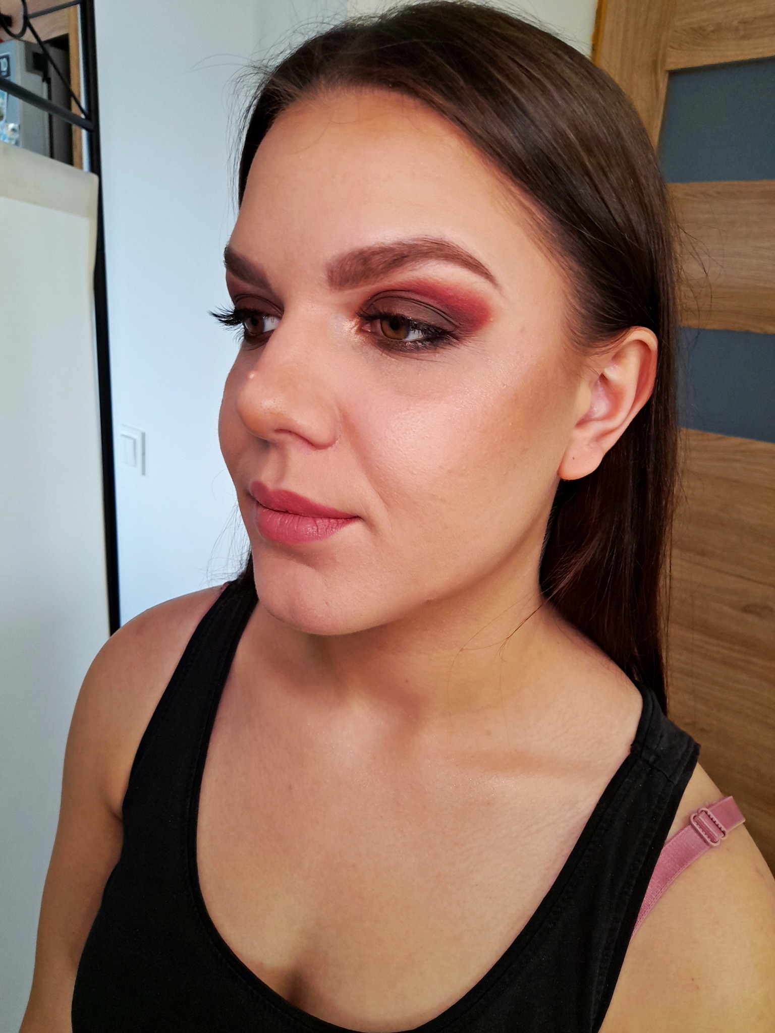 Portret kobiety z profesjonalnie wykonanym, intensywnym makijażem oczu w odcieniach bordo i brązu, z widocznymi sztucznymi rzęsami i delikatnie podkreślonymi ustami w kolorze różowym.