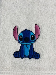 Biały ręcznik z niebieskim haftem postaci Stitch, wyraźne detale, delikatne cieniowanie, precyzyjne wykonanie, widoczna faktura materiału.
