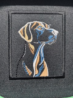 Czarny naszywka z wyhaftowanym wizerunkiem psa rasy wyżeł niemiecki krótkowłosy, umieszczona na ciemnoszarym tle materiału. Detal haftu.