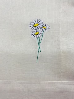 Delikatny, ręcznie wykonany motyw trzech białych stokrotek z żółtymi środkami, zdobiący jasną tkaninę. Subtelne detale podkreślają precyzję wykonania.