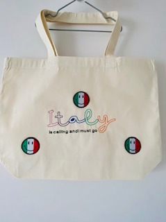 Ecru torba bawełniana z kolorowym napisem 'Italy is calling and I must go' oraz trzema naszywkami z flagą Włoch i uśmiechniętą buźką.