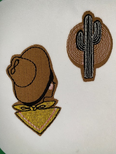 Wykonane techniką dekoracyjną aplikacje: kowboj w kapeluszu i bandana oraz kaktus na białym materiale. Detale podkreślone brązowymi nićmi.