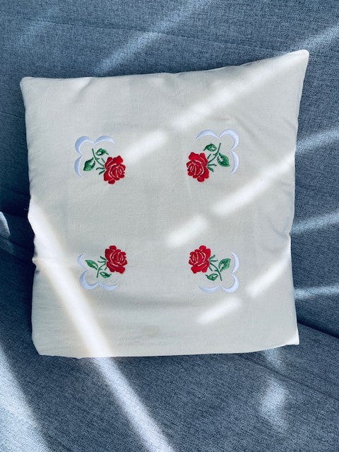 Kremowa poduszka z haftowanymi czerwonymi różami i białymi ornamentami w Łukowie. Delikatne światło podkreśla detale haftu i fakturę materiału.