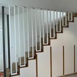 Nowoczesne schody drewniane z białymi, pionowymi elementami balustrady, zintegrowane z białą zabudową szaf wnękowych.