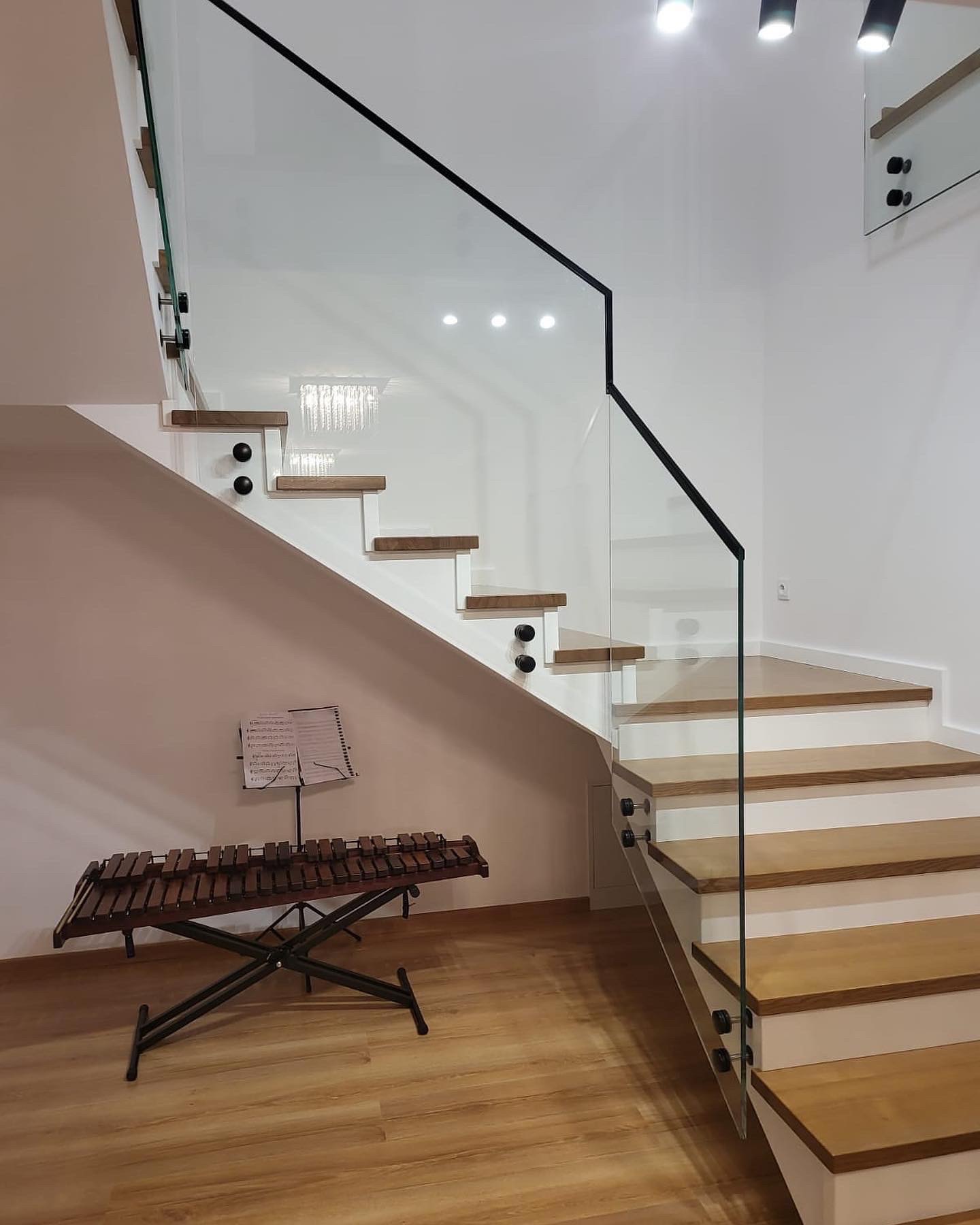 Nowoczesne schody drewniane z balustradą szklaną i czarnymi elementami mocującymi, obok ksylofon ze statywem na nuty