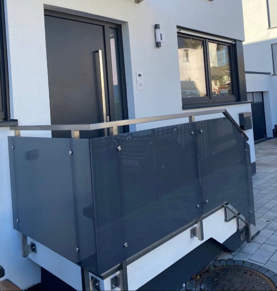 Nowoczesny balkon z szarą szklaną balustradą i nierdzewną poręczą, zamontowaną na białej elewacji budynku.