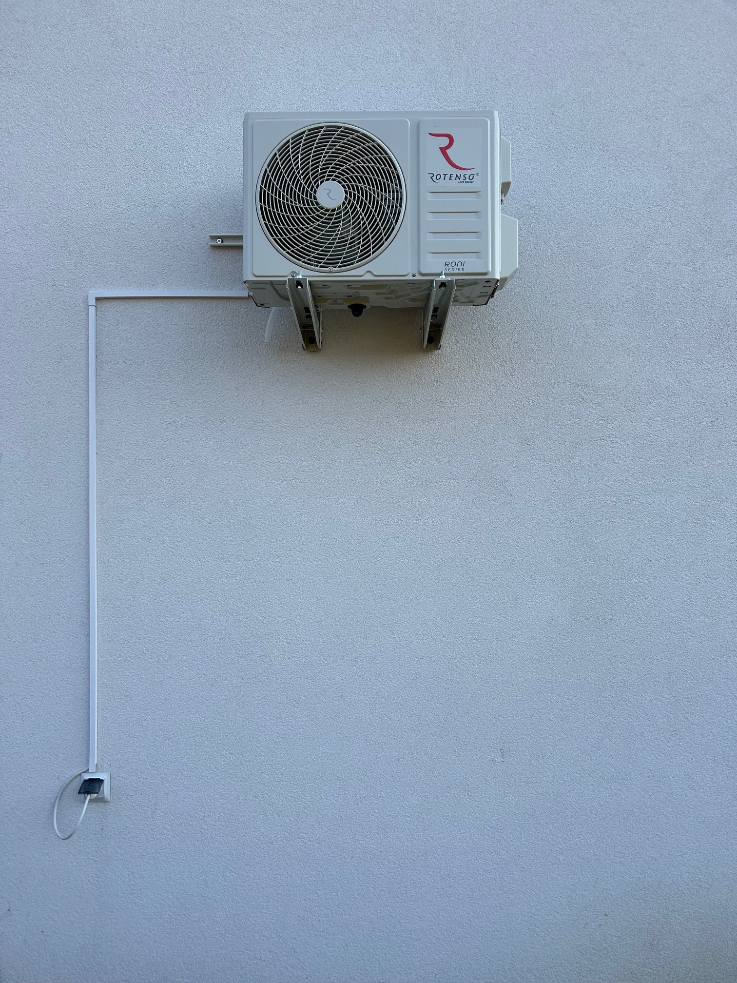 Zamontowana jednostka zewnętrzna klimatyzacji Rotenso na jasnej elewacji budynku, z widocznym okablowaniem i wspornikami montażowymi.