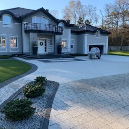 ABMax Alan Białecki - Rozległy podjazd z kostki brukowej prowadzący do nowoczesnego domu z balkonem, widoczna przyczepa z urządzeniem ciśnieniowym do czyszczenia.