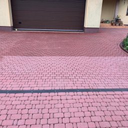 ABMax Alan Białecki - Częściowo wyczyszczona, czerwona kostka brukowa na podjeździe przed garażem, z widoczną różnicą w kolorze między czystą a brudną powierzchnią, oddzielona czarną kratką odpływową.