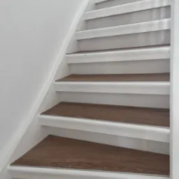 Białe schody z drewnopodobnymi panelami na stopniach, widok z dołu, akcent na detale wykończenia.